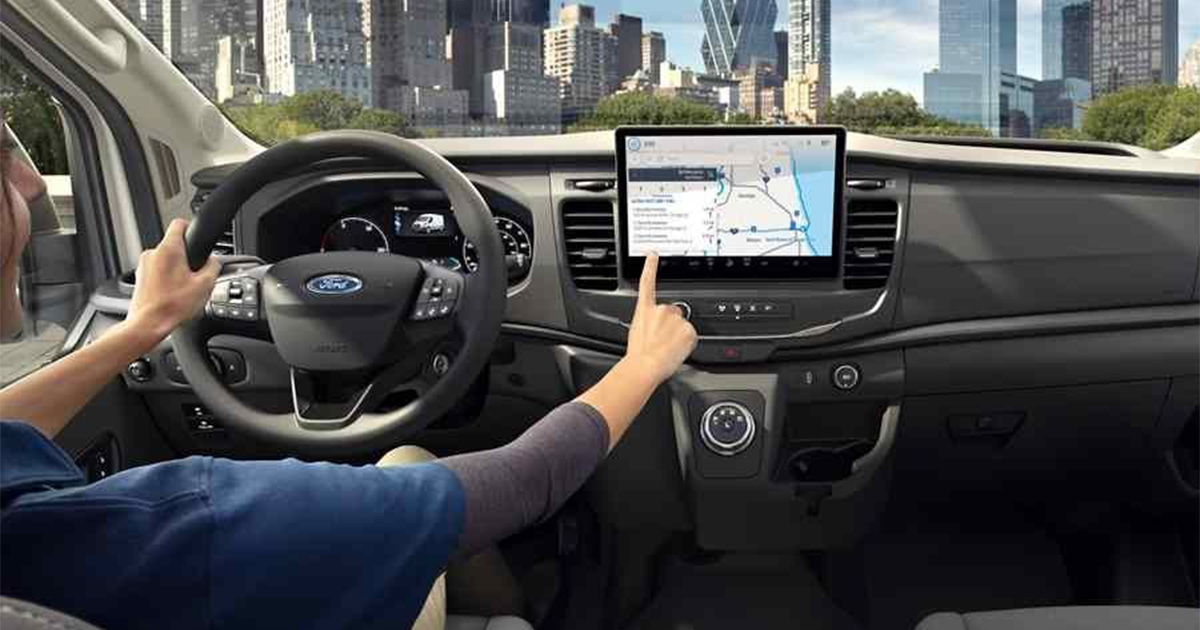 Ford Transit interior with driver's hand on touchscreen navigation system, city skyline in background