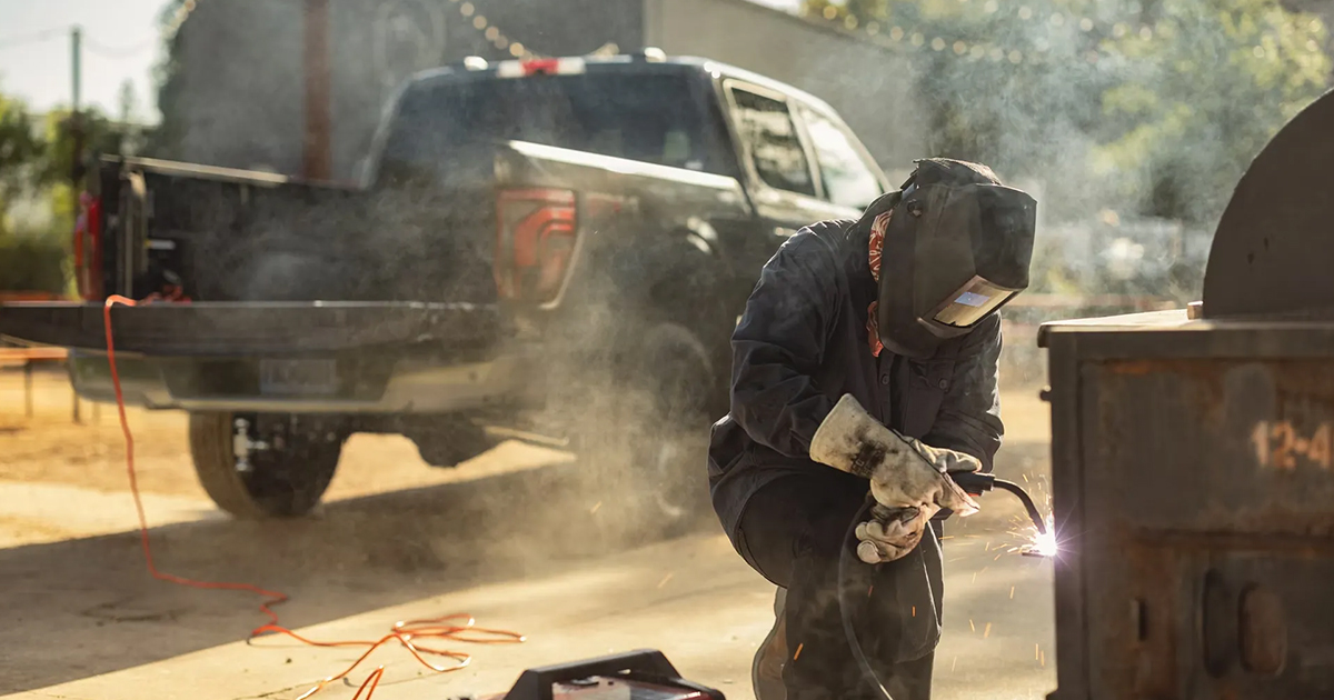 Welder in protective gear working with sparks near a Ford F-150 pickup truck in an industrial outdoor setting