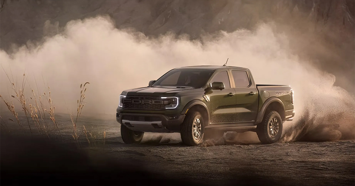 Ford Ranger Raptor in dark green, kicking up dust while driving off-road with rugged terrain in background