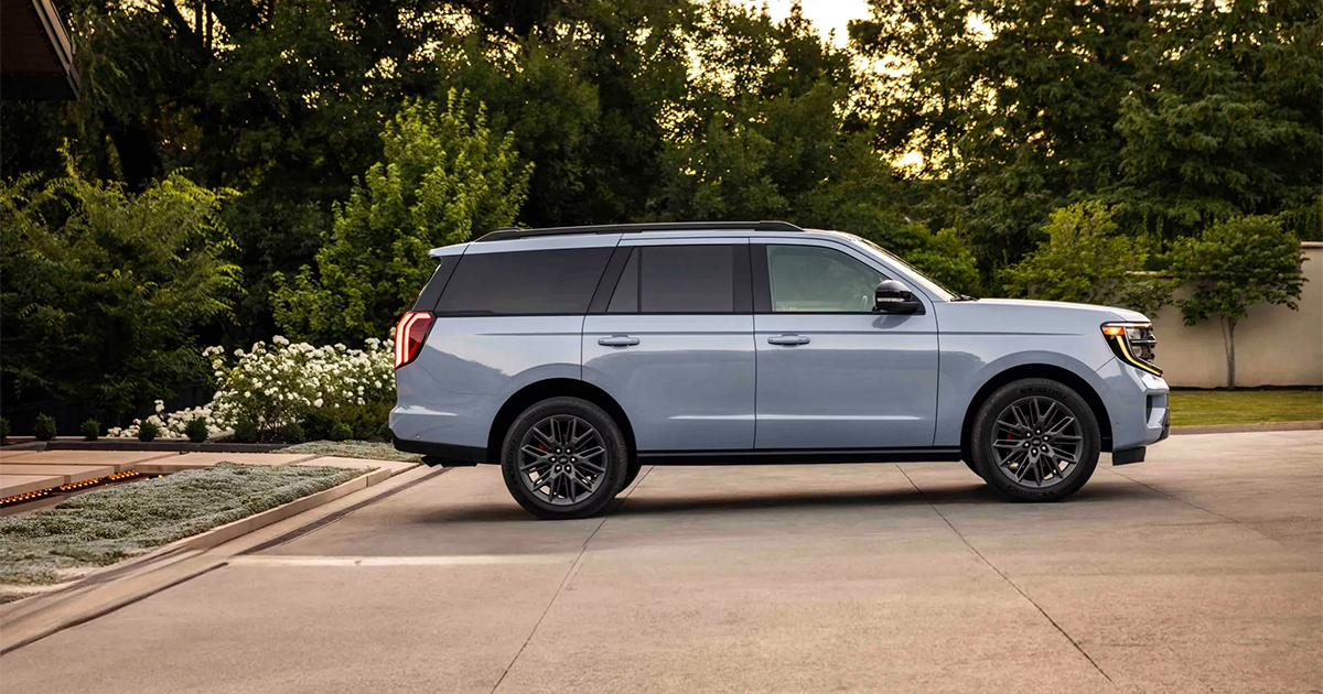 2024 Ford Expedition full-size SUV in silver, parked on concrete with lush green trees and white flowers in background