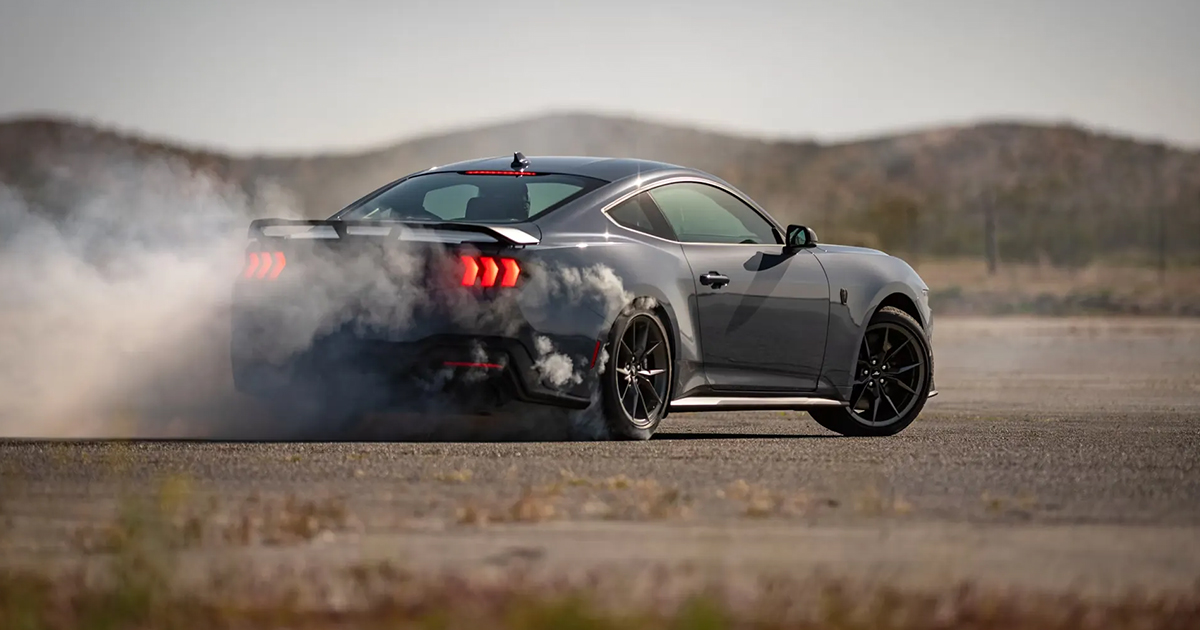 Dark gray Ford Mustang Dark Horse doing a burnout on desert road with tire smoke and mountain backdrop