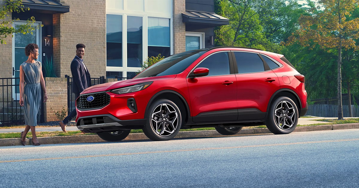 Red Ford Escape SUV parked on street with two people near modern brick building and trees