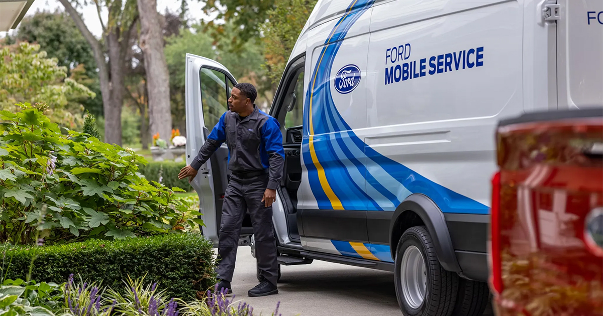Ford Mobile Service technician stepping out of white van with blue graphics, parked near landscaped garden