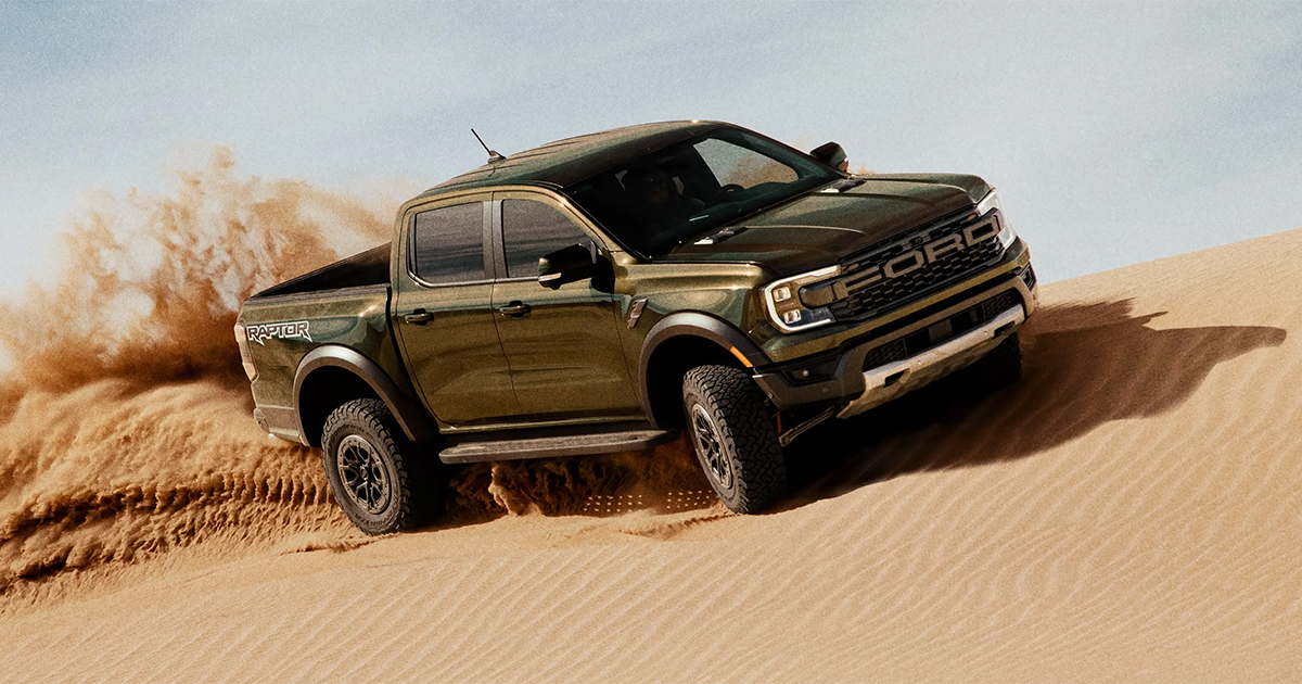 Ford Ranger Raptor driving through sandy desert terrain, kicking up dust with rugged off-road performance