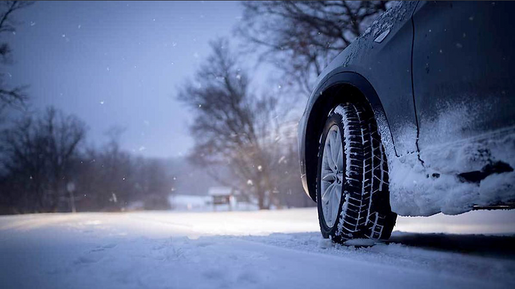Winter driving scene: Ford SUV tire with snow chains on snowy road, bare trees in background, showcasing vehicle traction in cold conditions