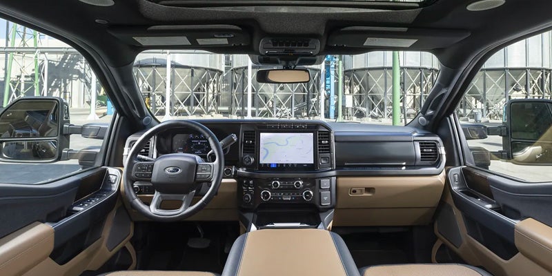 The tan and black interior dashboard of a Ford truck with a large infotainment screen, seen through the front windshield