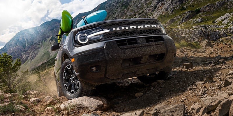 A dark gray Ford Bronco Sport with kayaks is rock crawling uphill
