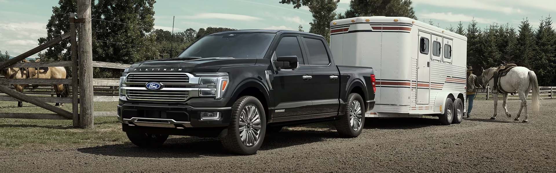A **black Ford F-150 Platinum pickup truck** towing a white horse trailer on a farm.