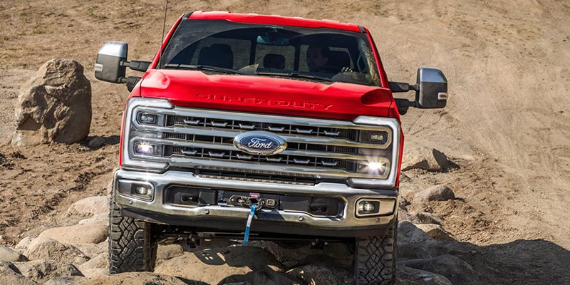 A red Ford Super Duty truck with a winch driving over rough, rocky terrain.