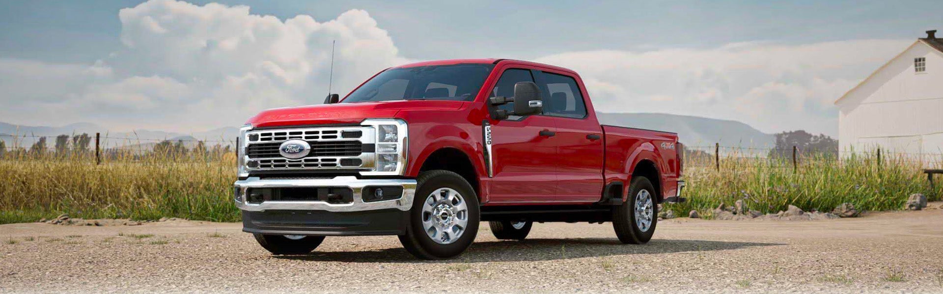 Red Ford Super Duty pickup truck parked in a gravel farm setting.