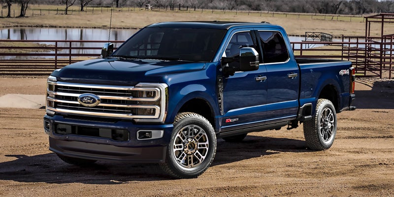 Dark blue Ford Super Duty crew cab pickup truck parked on a dirt road in a ranch or farm setting